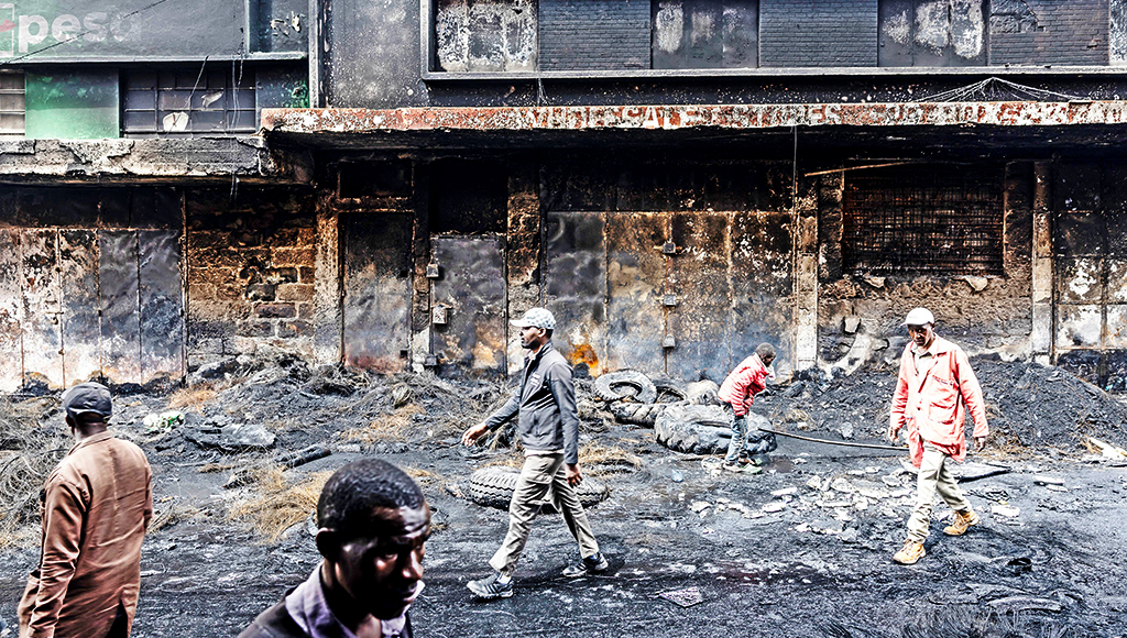 Residents walk past a shopping centre that was vandalized and torched during deadly protests marking one year since the storming of parliament in anti-tax demonstrations in Nairobi.